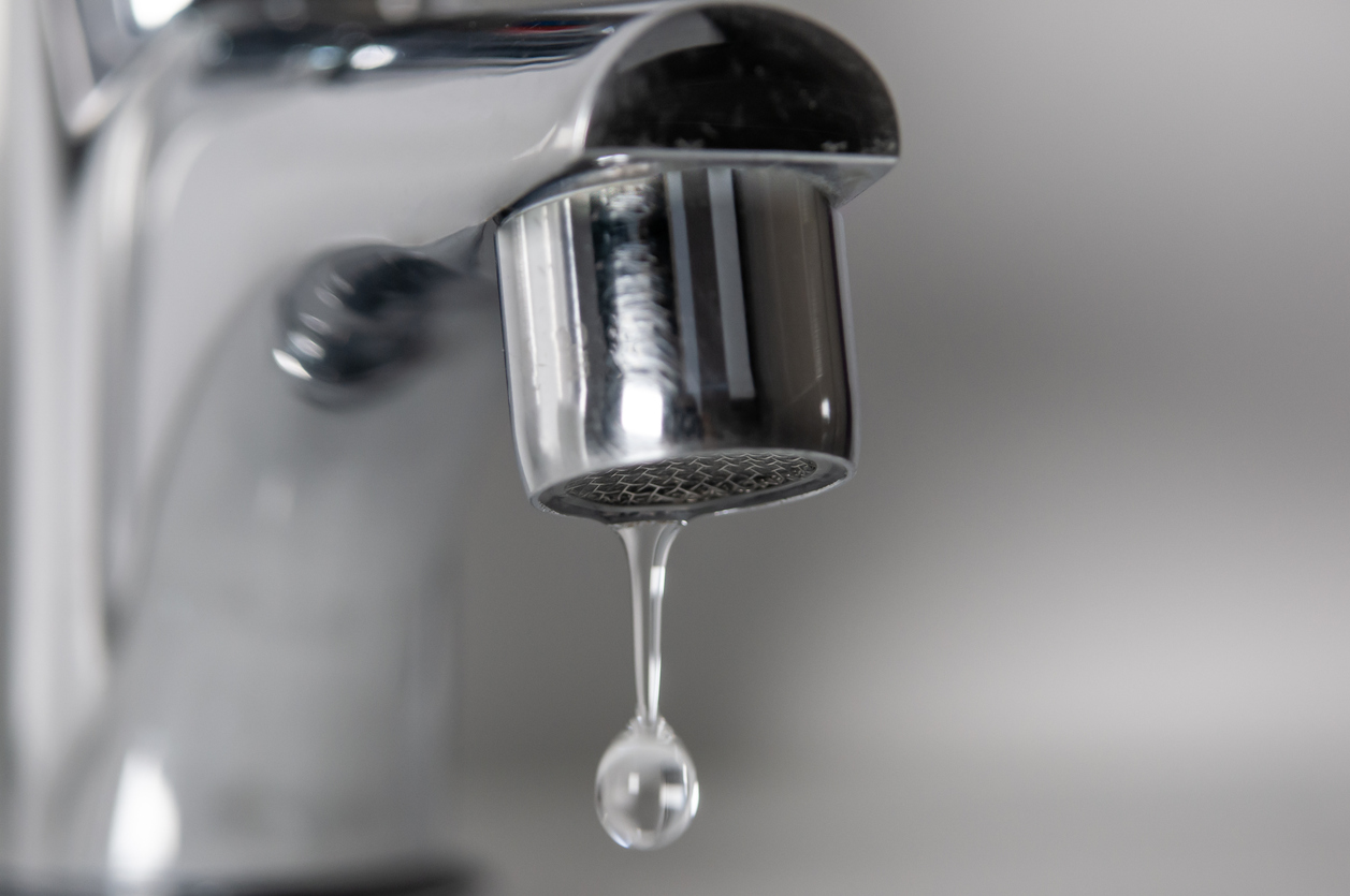 Macro photograph of a chrome faucet dripping water.
